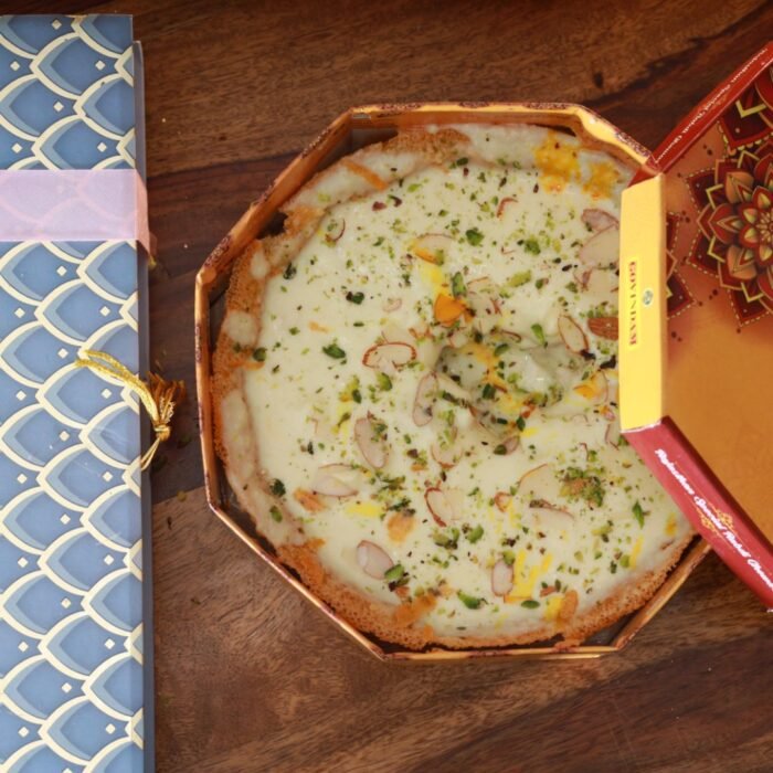 Golden disc-shaped Malai Ghewar topped with creamy rabri and pistachios on silver platter