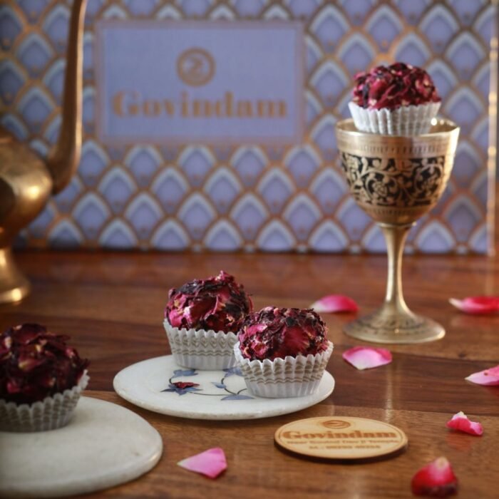 Pale pink rose laddus garnished with dried rose petals, arranged on a vintage floral plate