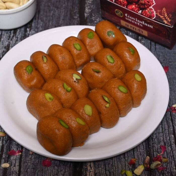 Assorted Rajasthani pedas in various shapes and sizes, decorated with saffron strands and pistachios