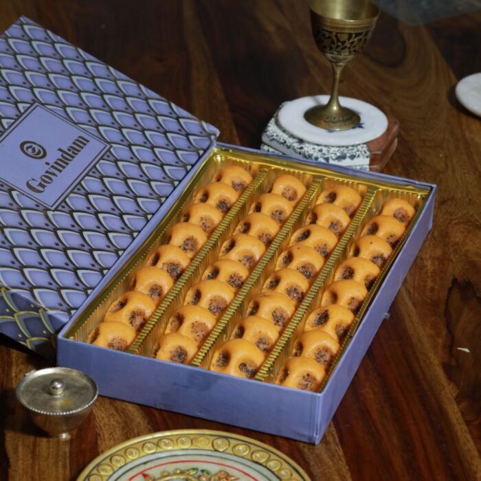 Golden-brown Rajasthani pedas with intricate designs pressed on top, arranged on a colorful Rajasthani thali