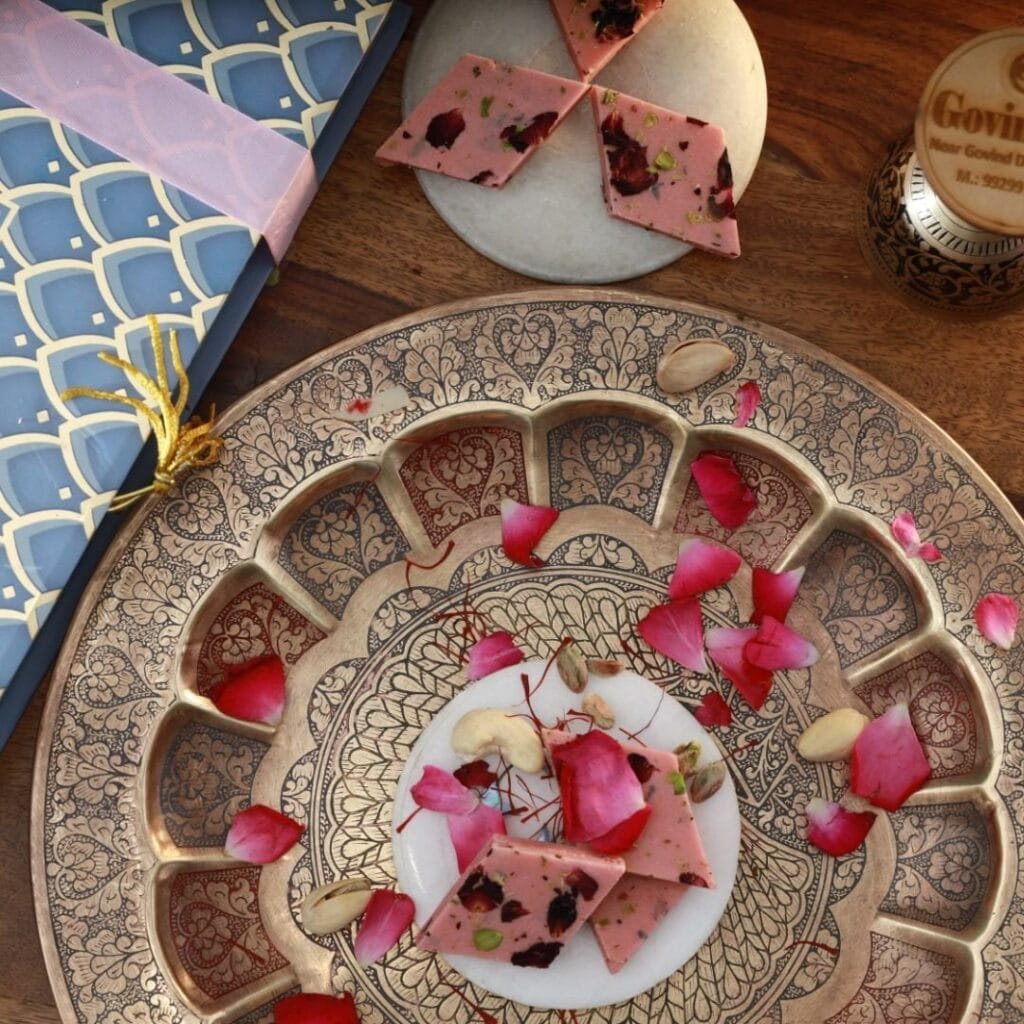 Rose katli pieces arranged in a mandala pattern with fresh rose petals and silver vark accents