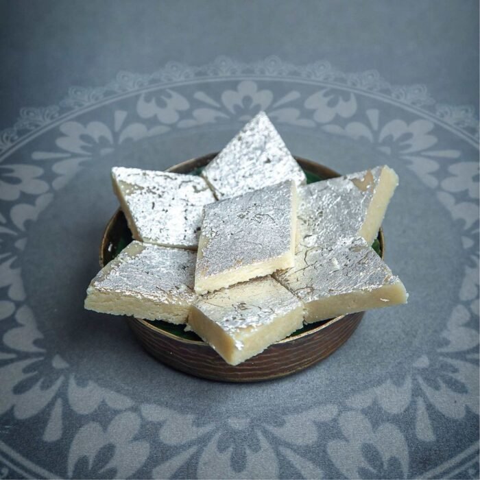 Diamond-shaped Kaju Katli pieces with silver vark topping arranged on a brass thali