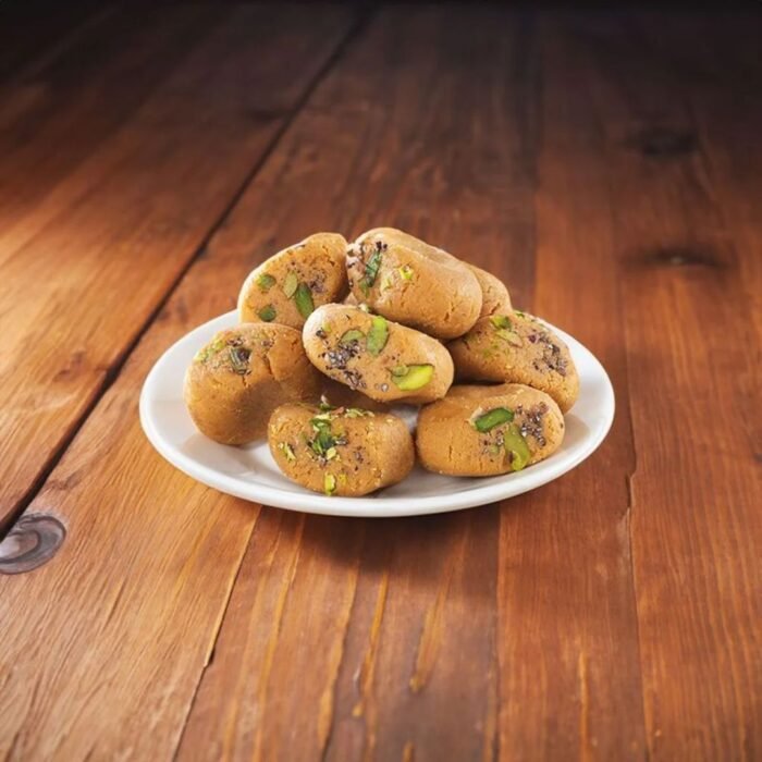 Golden-brown Mathura pedas with intricate floral designs pressed on top, arranged on a brass thali