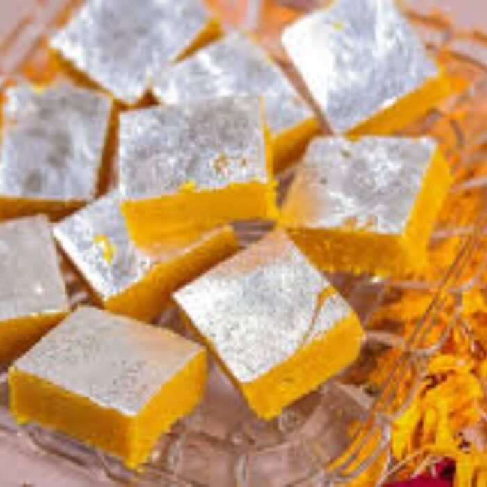 Golden-yellow mewa mango barfi squares garnished with slivered almonds on a brass thali