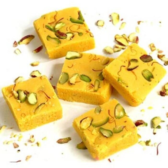 Assorted shapes of mewa kesar barfi arranged in a mandala pattern with edible gold leaf accents